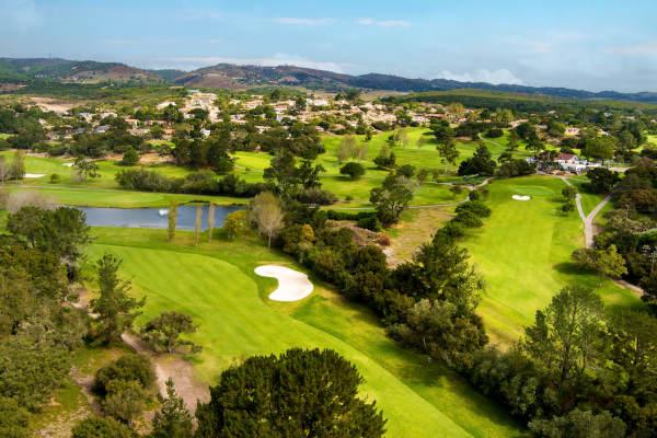 An expansive aerial view of a lush green golf course featuring sand bunkers and a water hazard near a residential community.